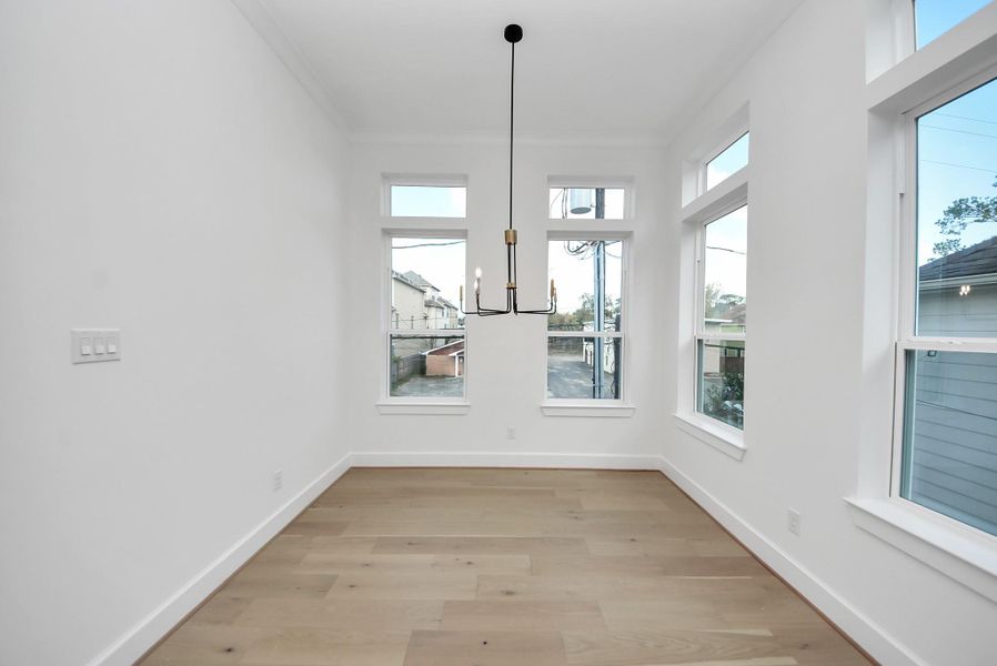 A bright dining area filled with natural light from large windows, complemented by hardwood floors and a modern chandelier—an inviting space for everyday meals and casual entertaining.
