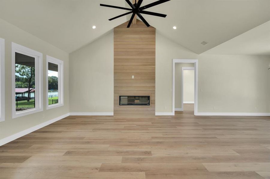 Unfurnished living room with ceiling fan, light hardwood / wood-style flooring, a fireplace, and high vaulted ceiling