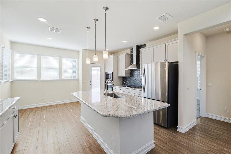 Kitchen featuring a center island with sink, sink, wall chimney exhaust hood, white cabinetry, and stainless steel appliances