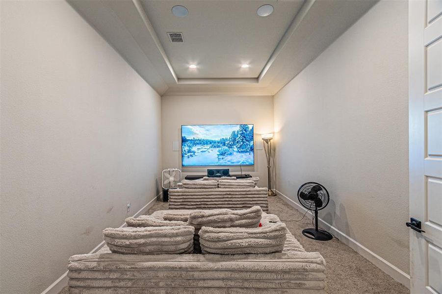 Dedicated media room featuring tray ceiling with recessed lighting, integrated ceiling speakers, and wall-mounted television