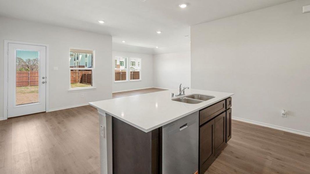 Kitchen island featuring a double-basin stainless steel sink with a chrome faucet, integrated dishwasher, and a light-toned countertop Kitchen island featuring a double-basin stainless steel sink with a chrome faucet, integrated dishwasher, and a light-toned countertop