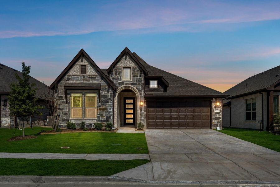 Stone exterior home with arched entry, two-car garage, and manicured front lawn at dusk