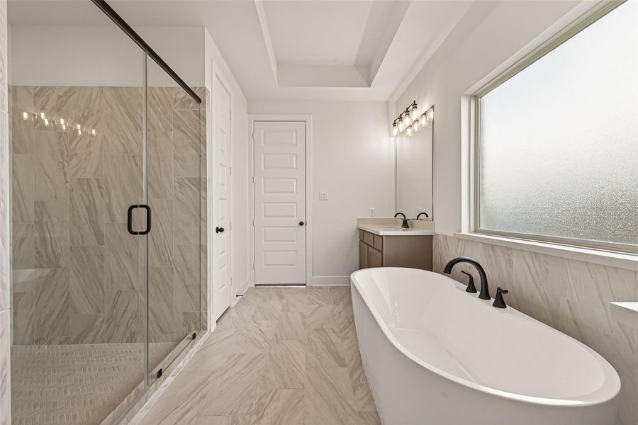 This bathroom features a spacious walk-in shower with glass doors, a sleek freestanding bathtub, and a large frosted window for natural light. The neutral tile and modern fixtures create a clean, elegant look.