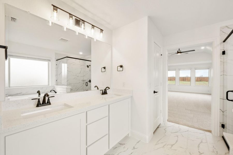 Master bathroom with double vanity, white quartz countertops, marble tile floors, and glass shower enclosure