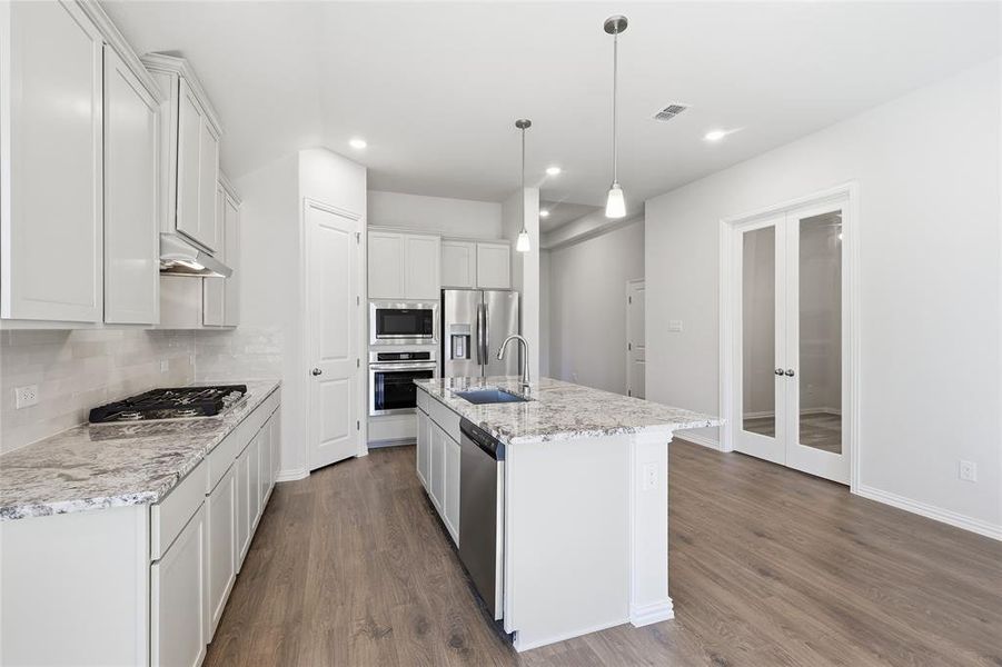 Kitchen with french doors, tasteful backsplash, stainless steel appliances, dark wood finished floors, and a center island with sink Kitchen with french doors, tasteful backsplash, stainless steel appliances, dark wood finished floors, and a center island with sink
