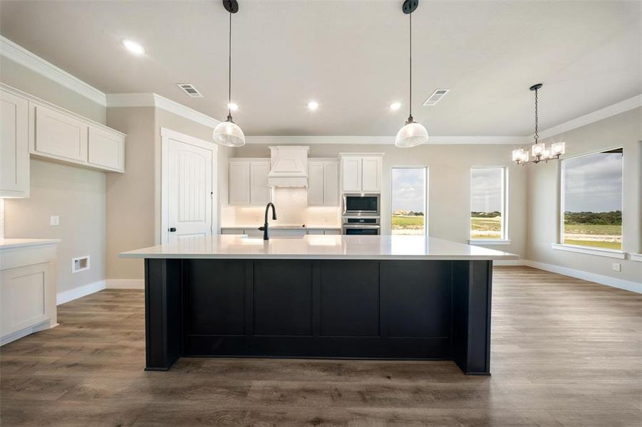Kitchen featuring ornamental molding, light countertops, white cabinets, a spacious island, and wood finished floors Kitchen featuring ornamental molding, light countertops, white cabinets, a spacious island, and wood finished floors