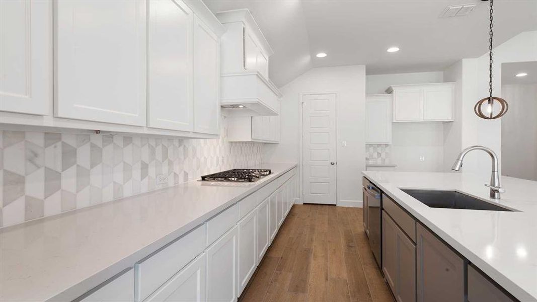 Kitchen with hanging light fixtures, appliances with stainless steel finishes, white cabinetry, light hardwood / wood-style flooring, and sink