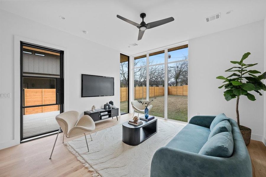 Living room featuring a wall of windows, light wood finished floors, and a ceiling fan