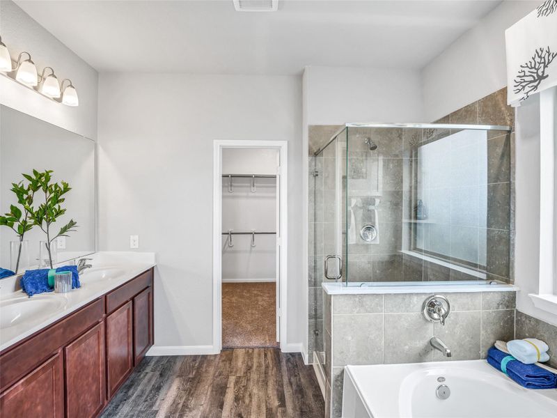 Escape to a spa-like oasis in this primary bathroom. Enjoy a walk-in shower with tile surround, a separate garden tub with custom detailing, and an elegant vanity featuring light countertops, modern hardware, and beautiful vanity lights. Experience luxury and relaxation in every detail. Sample photo of completed home with similar floor plan. Actual colors and selections may vary. Escape to a spa-like oasis in this primary bathroom. Enjoy a walk-in shower with tile surround, a separate garden tub with custom detailing, and an elegant vanity featuring light countertops, modern hardware, and beautiful vanity lights. Experience luxury and relaxation in every detail. Sample photo of completed home with similar floor plan. Actual colors and selections may vary.
