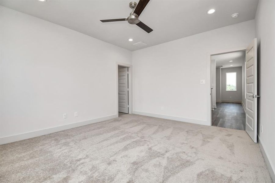 Spacious primary bedroom with neutral color walls and carpeted flooring, featuring a ceiling fan and recessed lighting.