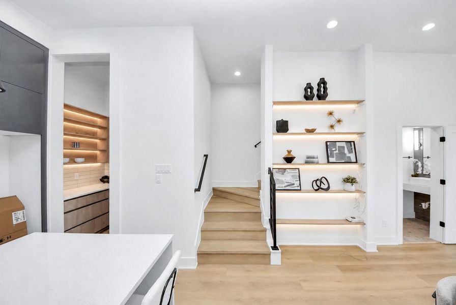 Second-floor kitchen area featuring custom display shelving, light wood stairs, and easy access to the powder room.