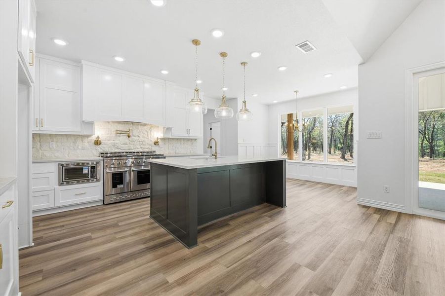 Two tone kitchen with stainless steel appliances, a center island with sink, pendant lighting, light stone countertops, and tasteful backsplash