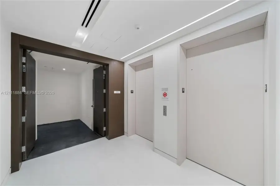 Elevator landing featuring dual elevator doors, stone flooring, recessed ceiling lighting, and a dark wood-finish entryway frame Elevator landing featuring dual elevator doors, stone flooring, recessed ceiling lighting, and a dark wood-finish entryway frame