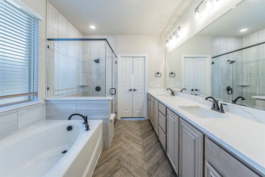 Bathroom featuring a large soaking tub, glass-enclosed shower with a built-in bench, dual vanity with undermount sinks, and herringbone wood-finish flooring