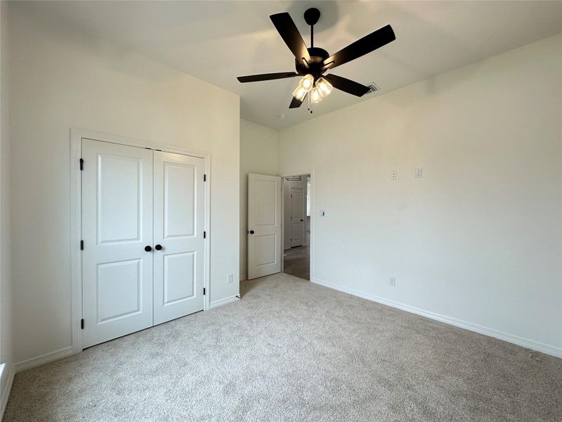 Spacious room featuring neutral carpet flooring, a ceiling fan with integrated lighting, clean white walls, and white bi-fold doors with black hardware