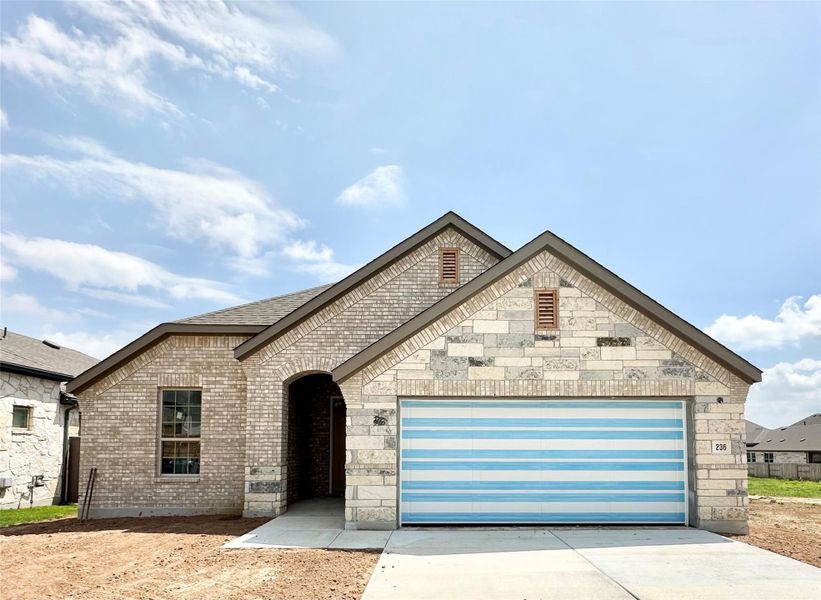 French country inspired facade featuring concrete driveway, a garage, brick siding, and roof with shingles French country inspired facade featuring concrete driveway, a garage, brick siding, and roof with shingles