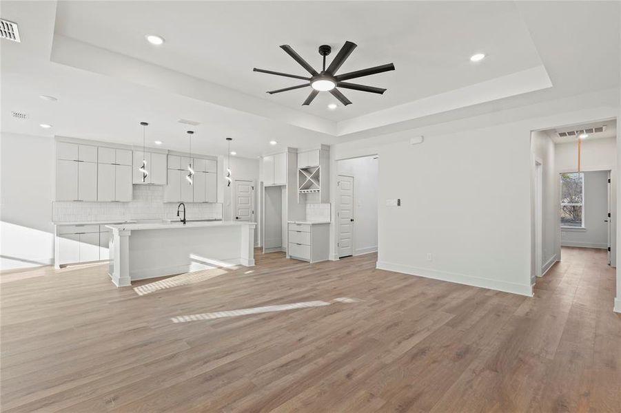 Unfurnished living room with light wood-type flooring, a tray ceiling, visible vents, and ceiling fan