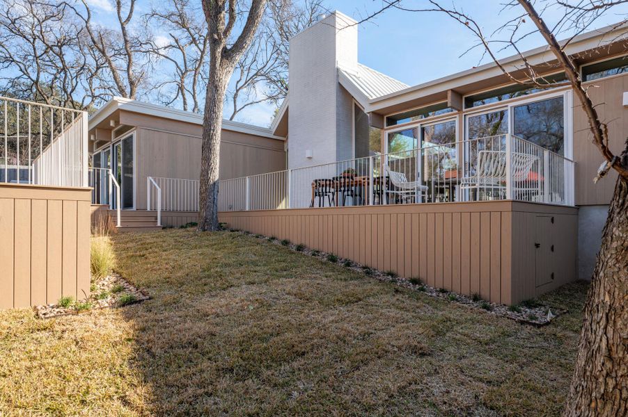 Back of property with a lawn, a chimney, a deck, and a sunroom