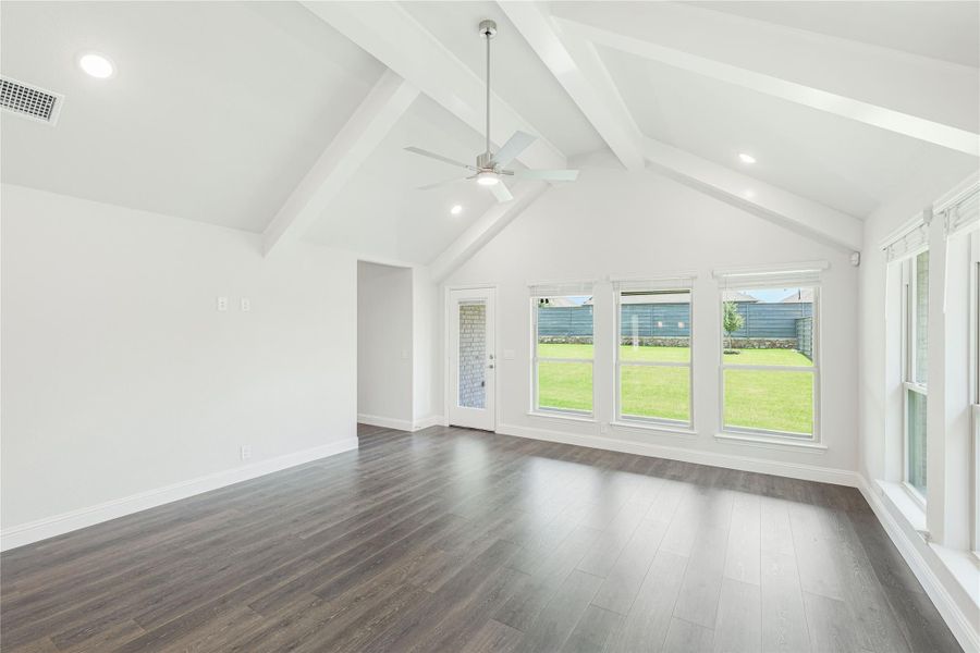 Open living room with vaulted beamed ceiling, ceiling fan, dark hardwood floors, and large windows overlooking backyard Open living room with vaulted beamed ceiling, ceiling fan, dark hardwood floors, and large windows overlooking backyard