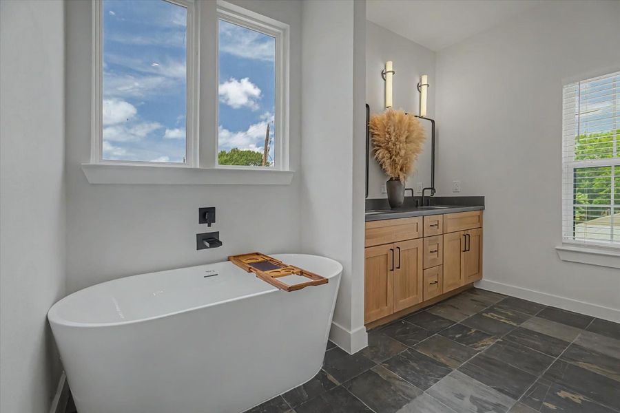 Primary bathroom featuring a soaking tub, slate flooring, and dual sinks.