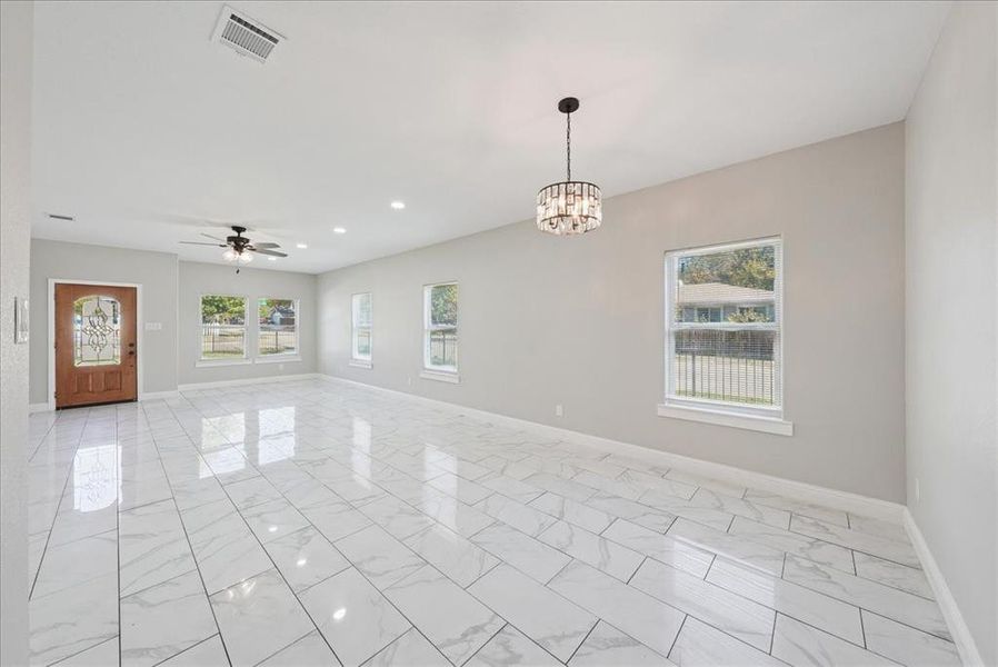 Spare room featuring light marble finish flooring, a ceiling fan, healthy amount of natural light, recessed lighting, and a chandelier
