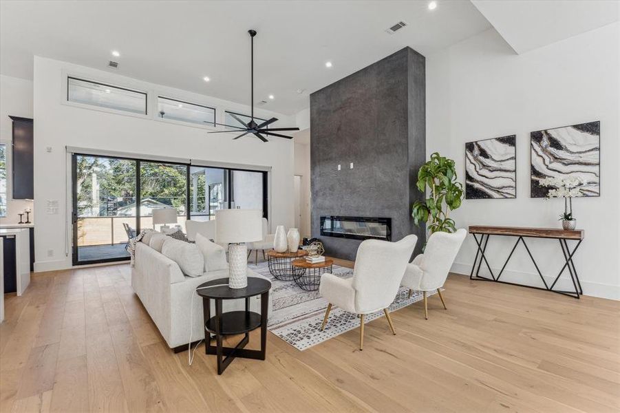 This family room features high ceilings, a dark accent wall with a built-in linear fireplace, large sliding glass doors opening to an outdoor space, and light wood flooring throughout.