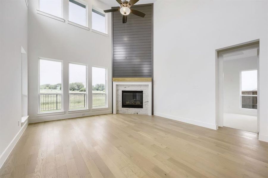 Open concept living area featuring a two-story ceiling, light wood-finish flooring, and a contemporary fireplace with a marble surround and wood mantel