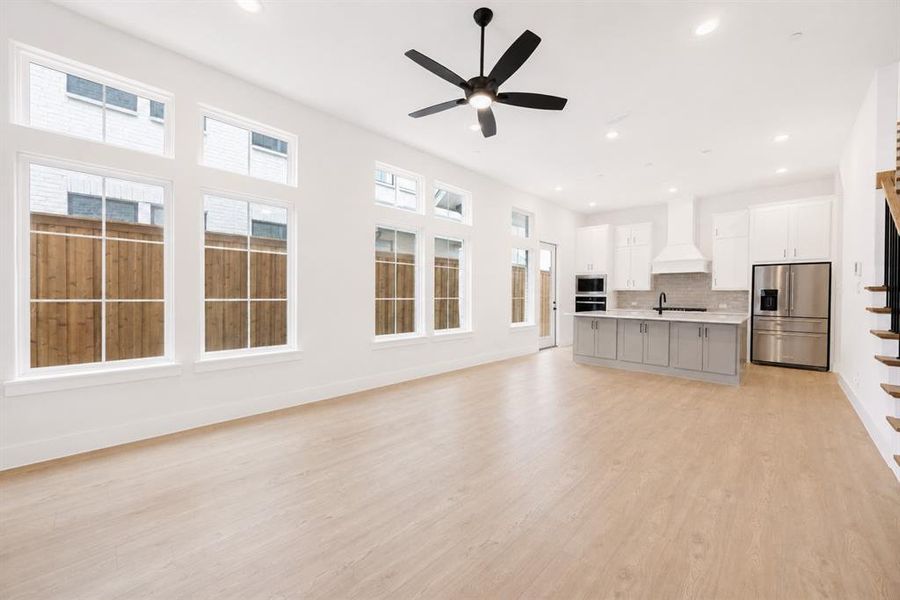 Open-concept living area featuring wood-finish flooring, a contemporary ceiling fan, recessed lighting, and an expansive window array