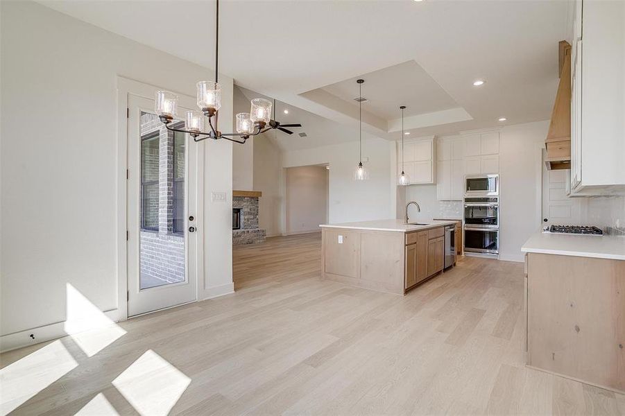 Kitchen featuring double wall oven, stainless steel microwave, an island with sink, sink, and a tray ceiling