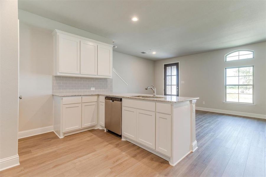 Kitchen with white cabinetry, dishwasher, sink, backsplash, and kitchen peninsula