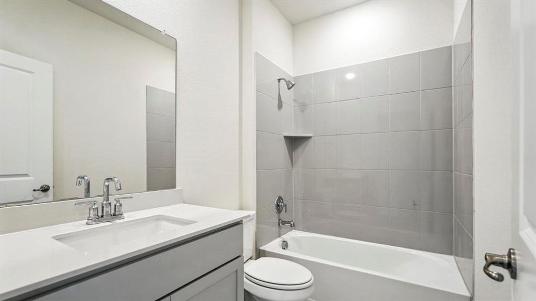 Bathroom featuring a single vanity with an integrated sink, polished chrome faucet, a large frameless mirror, and a tub-shower combination with gray subway tile surround and a built-in shower niche
