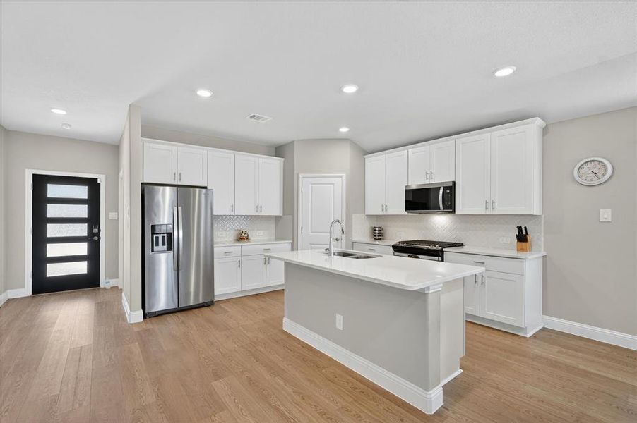 Open-concept kitchen with a central island, white shaker cabinetry, stainless steel appliances, and wood-finish flooring Open-concept kitchen with a central island, white shaker cabinetry, stainless steel appliances, and wood-finish flooring