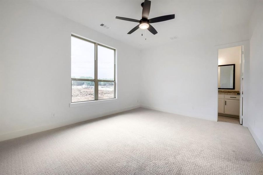 This inviting room features soft carpeting, a ceiling fan for comfort, and a large window providing natural light
