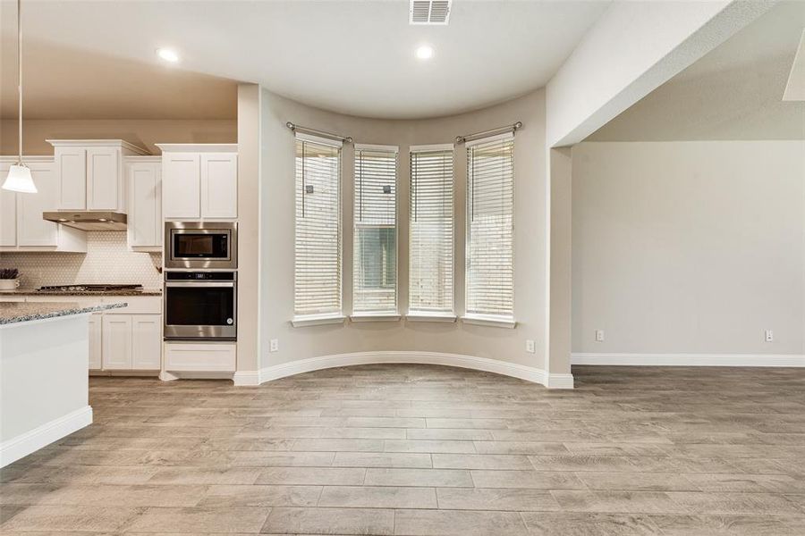 Kitchen with white cabinetry, decorative light fixtures, tasteful backsplash, appliances with stainless steel finishes, and light wood-style flooring