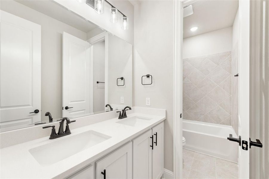 Bathroom with double sink vanity, white cabinets, black fixtures, and tiled tub-shower combo Bathroom with double sink vanity, white cabinets, black fixtures, and tiled tub-shower combo