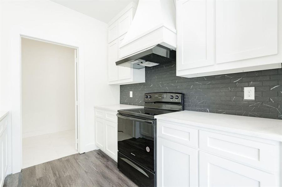 Kitchen with white cabinetry, electric range, and custom exhaust hood