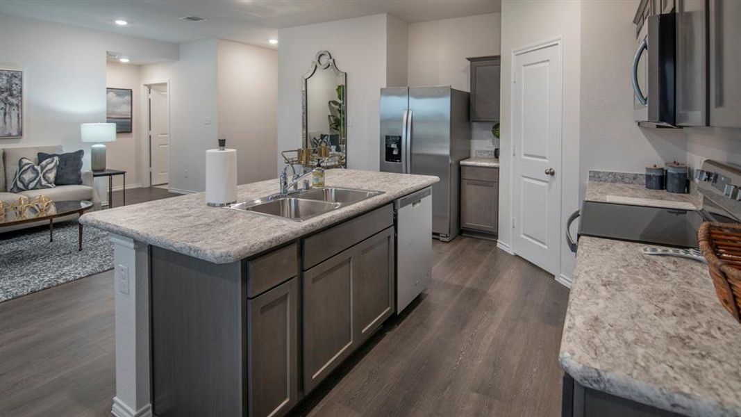 Kitchen featuring light countertops, stainless steel appliances, open floor plan, an island with sink, and dark wood-style floors