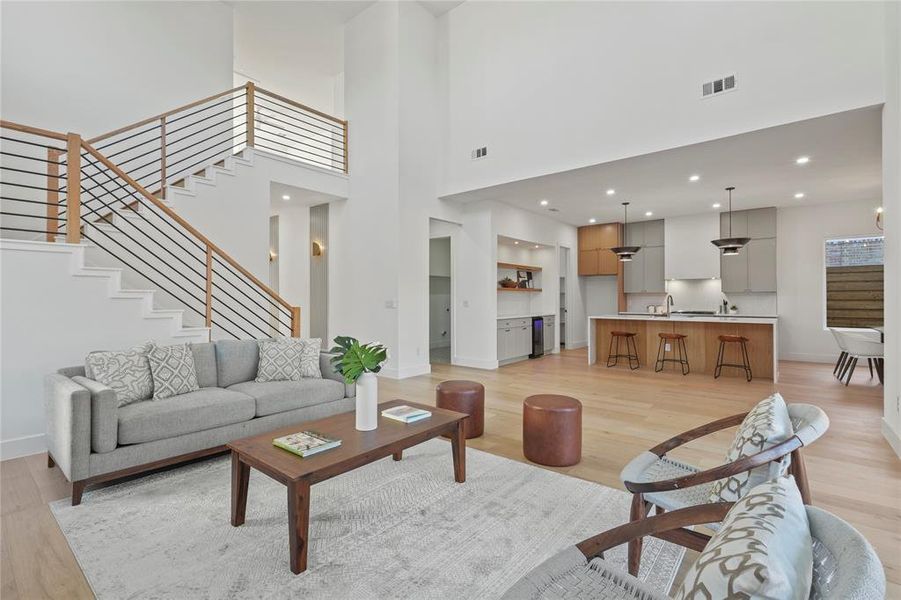 Living room with light wood-type flooring, a towering ceiling, stairs, and recessed lighting
