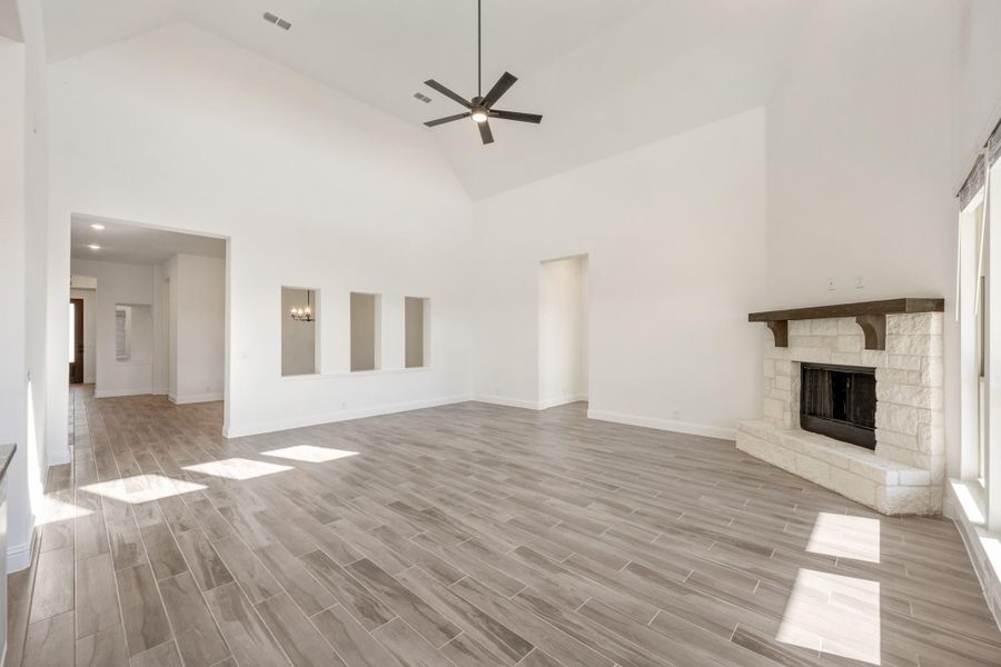 Open living room with vaulted ceiling, stone fireplace, wood-look tile floors, and ceiling fan Open living room with vaulted ceiling, stone fireplace, wood-look tile floors, and ceiling fan
