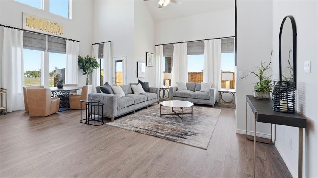 Expansive living area featuring vaulted ceilings, wood-finish flooring, a wall of large windows, and a built-in console table with an arched mirror Expansive living area featuring vaulted ceilings, wood-finish flooring, a wall of large windows, and a built-in console table with an arched mirror
