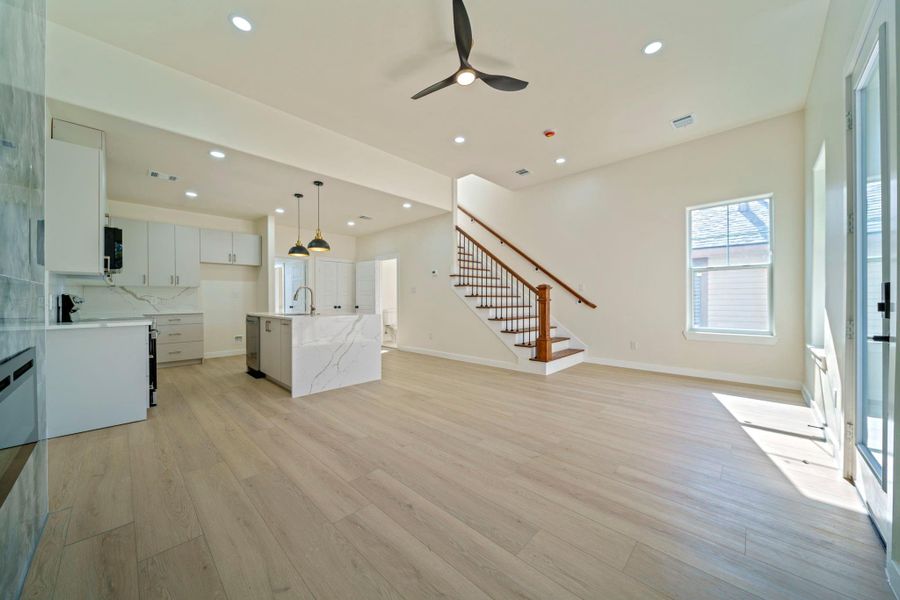 This photo showcases a bright, open-concept living area with light LVP flooring and ample natural light. The modern kitchen features sleek white cabinetry, quartz countertops, and an island with pendant lighting. A stylish staircase with wooden accents leads to the upper level. This photo showcases a bright, open-concept living area with light LVP flooring and ample natural light. The modern kitchen features sleek white cabinetry, quartz countertops, and an island with pendant lighting. A stylish staircase with wooden accents leads to the upper level.