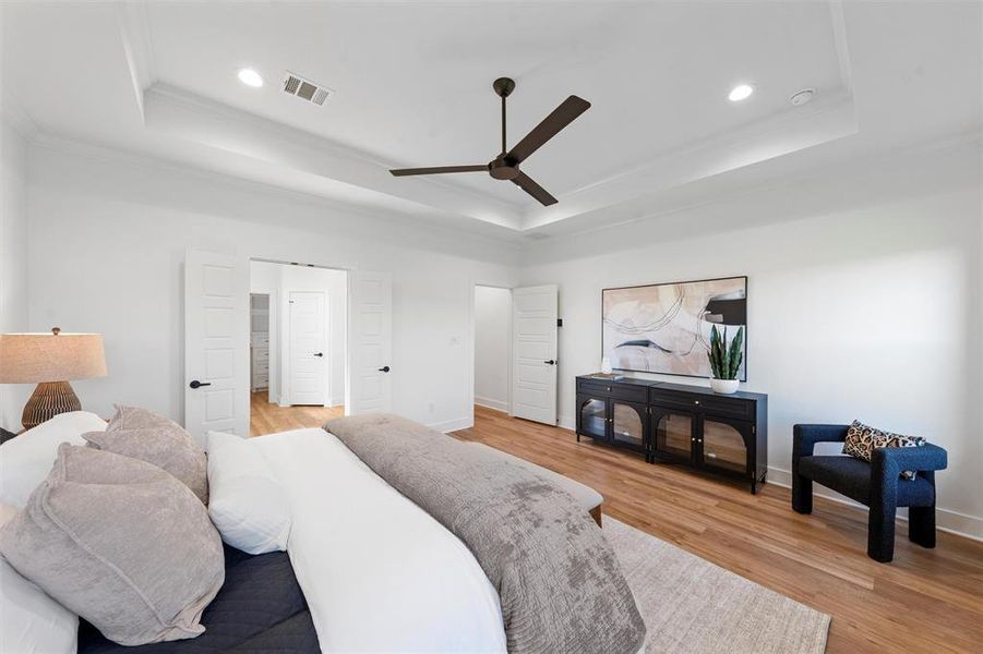 Bedroom with a tray ceiling, crown molding, recessed lighting, light wood finished floors, and a ceiling fan