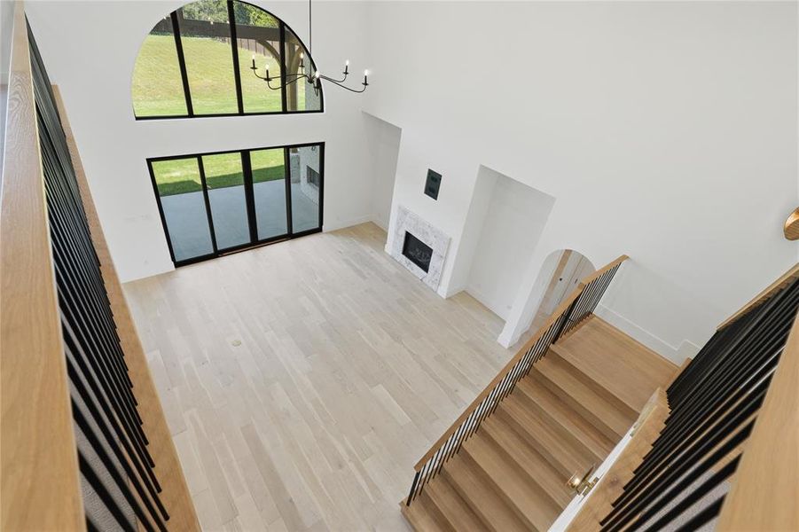 Vaulted living space featuring an arched transom window, sliding glass doors, a chandelier, a fireplace with a stone surround, and wood-finish flooring