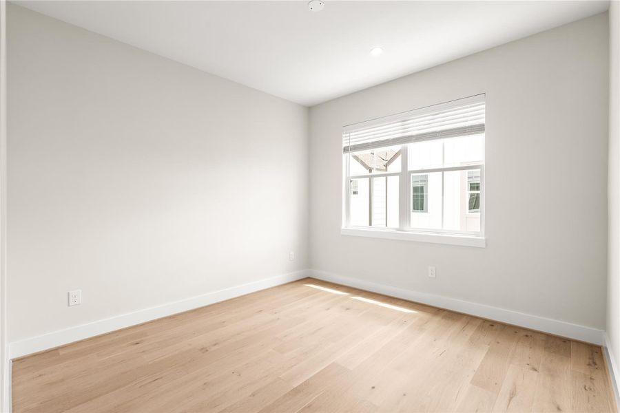A generously sized secondary bedroom with engineered wood flooring, a large window, and plenty of flexibility for guests, a home office, or additional living space.