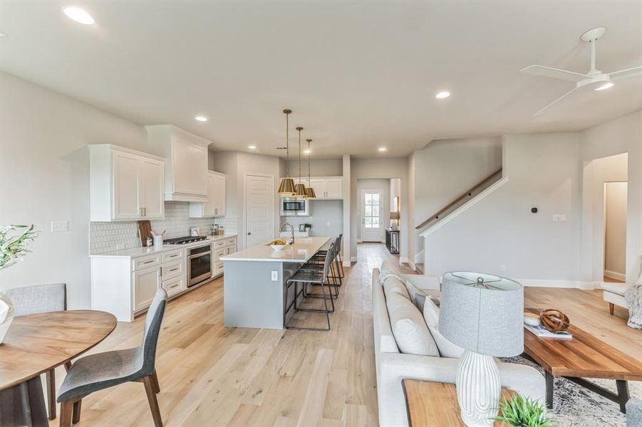 Kitchen with light hardwood / wood-style flooring, decorative backsplash, a center island with sink, and stainless steel appliances