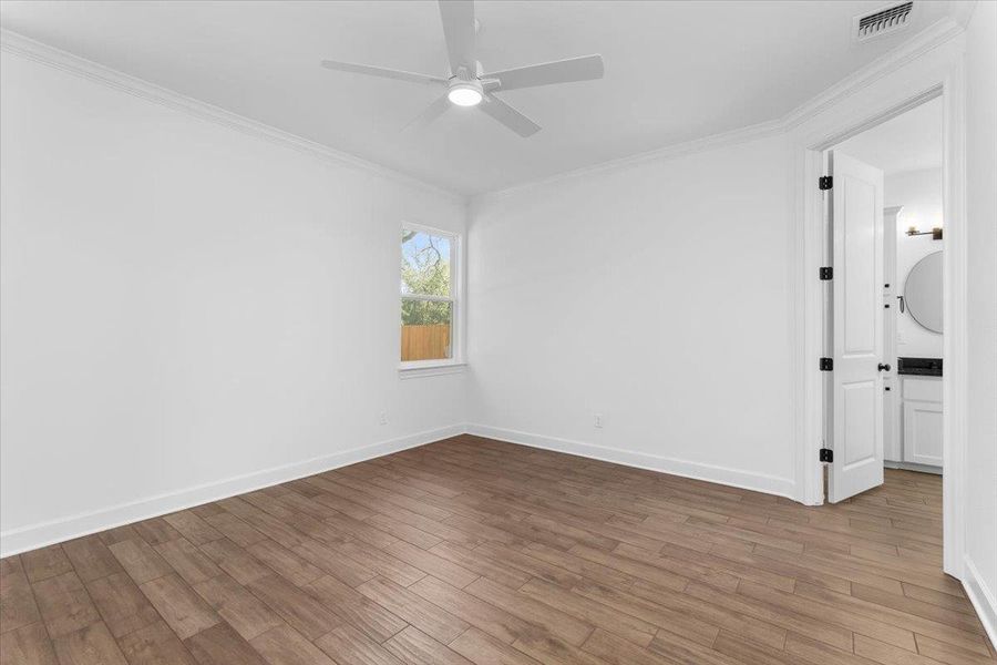 Empty room with ornamental molding, wood finished floors, a ceiling fan, and baseboards Empty room with ornamental molding, wood finished floors, a ceiling fan, and baseboards