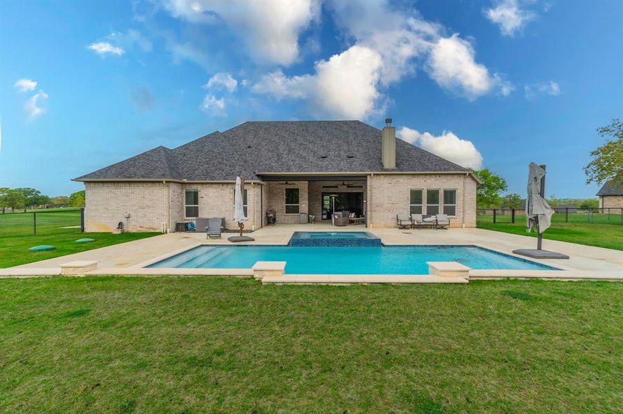 Rear view of property with a fenced backyard, a patio area, brick siding, a chimney, and a pool with connected hot tub Rear view of property with a fenced backyard, a patio area, brick siding, a chimney, and a pool with connected hot tub