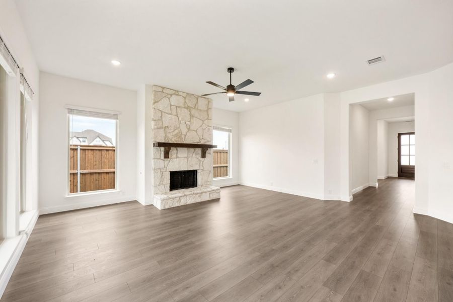 Open living room with floor-to-ceiling stone fireplace, hardwood floors, and ceiling fan