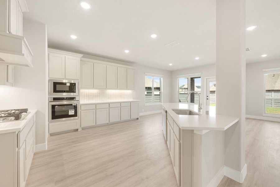 Open kitchen with white cabinets, stainless steel appliances, island with sink, and light wood floors