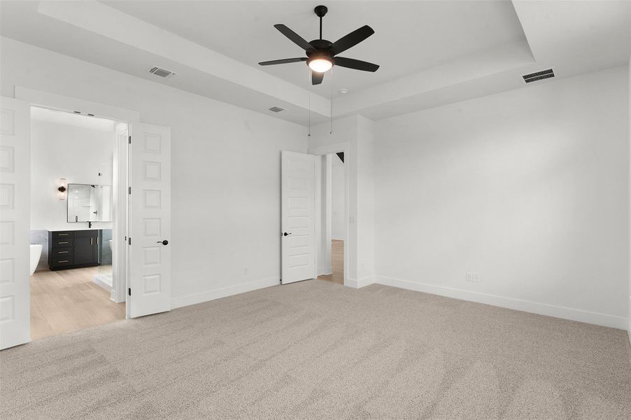 Unfurnished bedroom featuring a tray ceiling, light colored carpet, ceiling fan, and connected bathroom